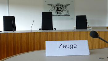 Bild mit Blick auf die Richterbank eines Sitzungssaales im Landesarbeitsgericht Baden-Württemberg und im Hintergrund an der Wand das Landeswappen.
